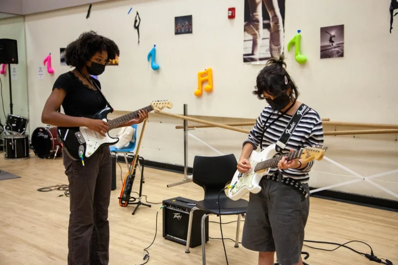 Two people practicing guitar while wearing masks.