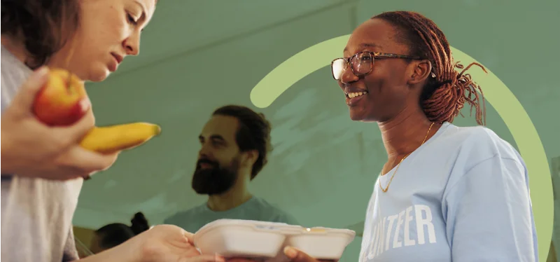 A smiling nonprofit volunteer hands food to a recipient at a community service event