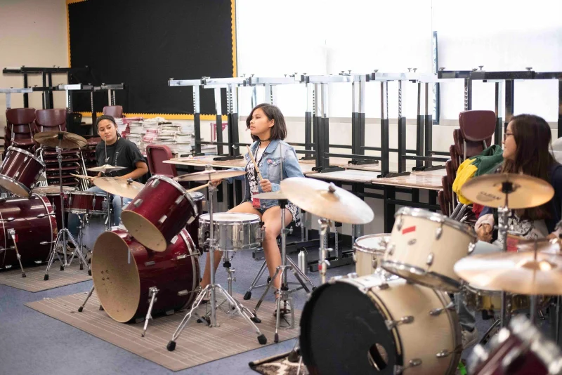 Three young people practicing playing the drums in a classroom.